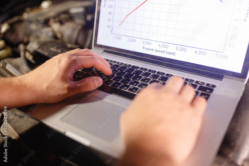 Closeup hands of mechanic with the help of diagnostic machines is ready for use with the car. Laptop torque figures and horsepower is the engine of the vehicle for diagnostics and configuration. Closeup hands of mechanic with the help of diagnostic machines is ready for use with the car. Laptop torque figures and horsepower is the engine of the vehicle for diagnostics and configuration.