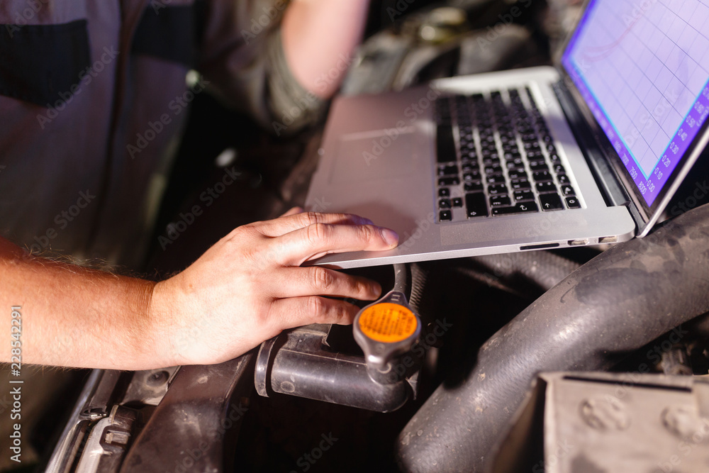 Closeup hands of mechanic with the help of diagnostic machines is ready for use with the car. Laptop torque figures and horsepower is the engine of the vehicle for diagnostics and configuration. Closeup hands of mechanic with the help of diagnostic machines is ready for use with the car. Laptop torque figures and horsepower is the engine of the vehicle for diagnostics and configuration.