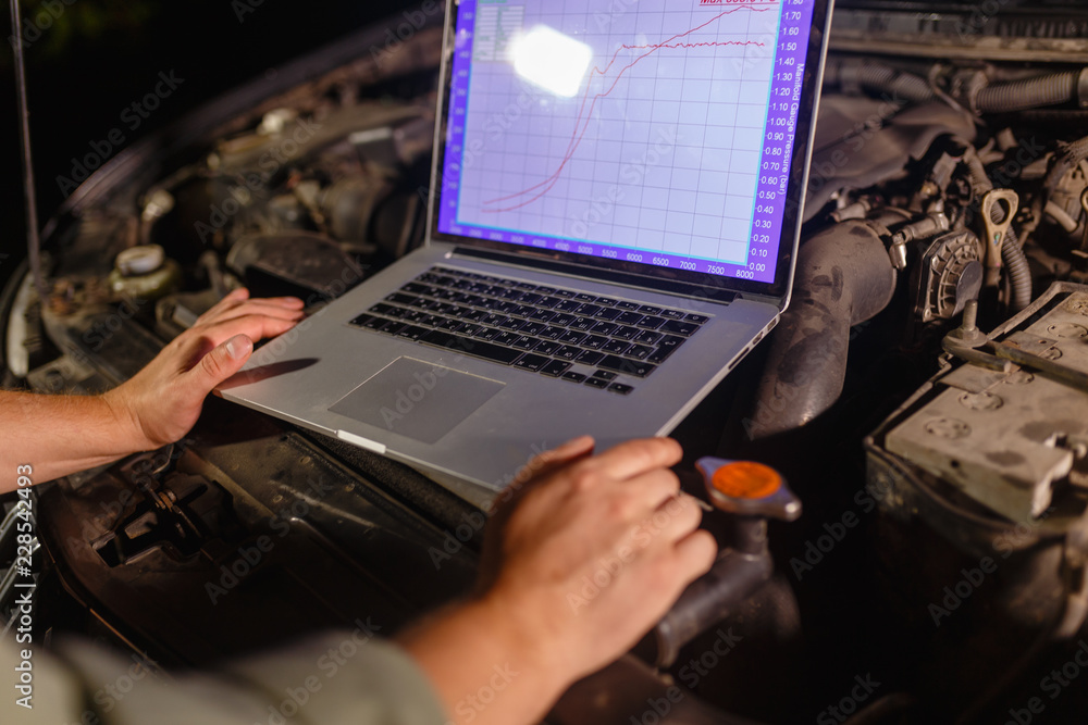 Closeup hands of mechanic with the help of diagnostic machines is ready for use with the car. Laptop torque figures and horsepower is the engine of the vehicle for diagnostics and configuration.