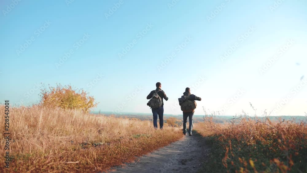 Two men traveler hiking with backpacks are walking along the path climbing into the mountains. slow motion video. Tourist Hipster Hiker traveler on background view blue sky clouds go hiking trip Two men traveler hiking with backpacks are walking along the path climbing into the mountains. slow motion video. Tourist Hipster Hiker traveler on background view blue sky clouds go hiking trip