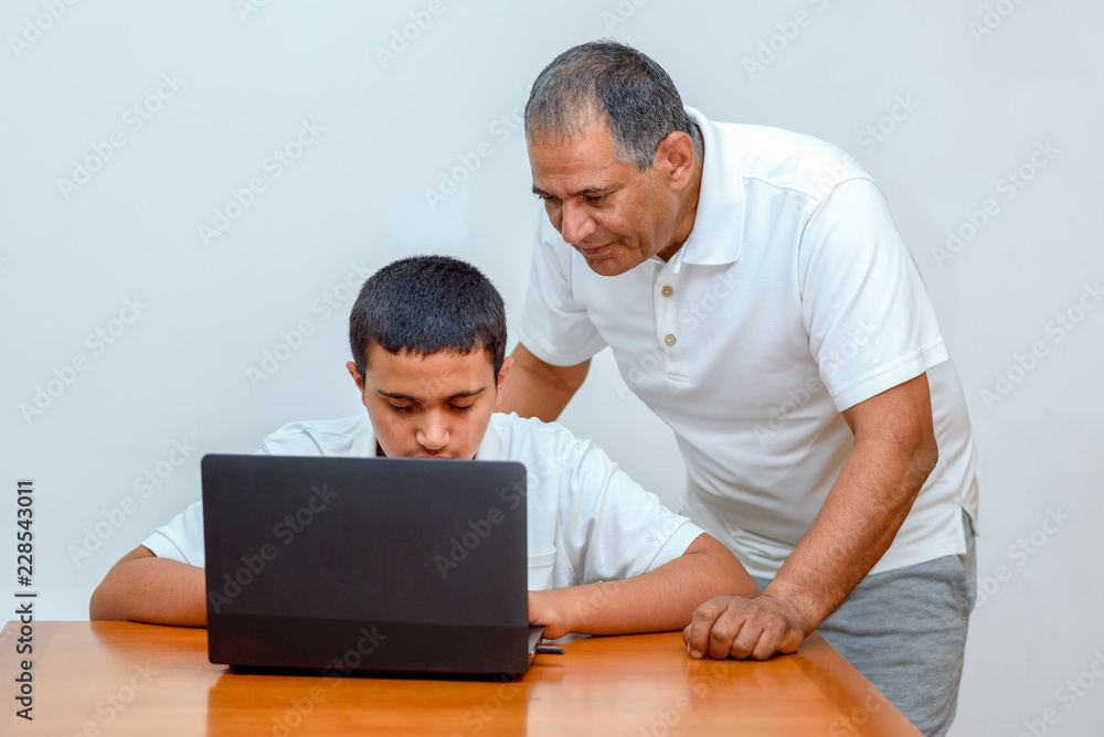 Senior Father and teenage son using laptop. Boy and dad with deeper skin tones working with computer. Happy family old grandfather and grandson on laptop.Elderly teacher trainer and teen pupil boy. Senior Father and teenage son using laptop. Boy and dad with deeper skin tones working with computer. Happy family old grandfather and grandson on laptop.Elderly teacher trainer and teen pupil boy.