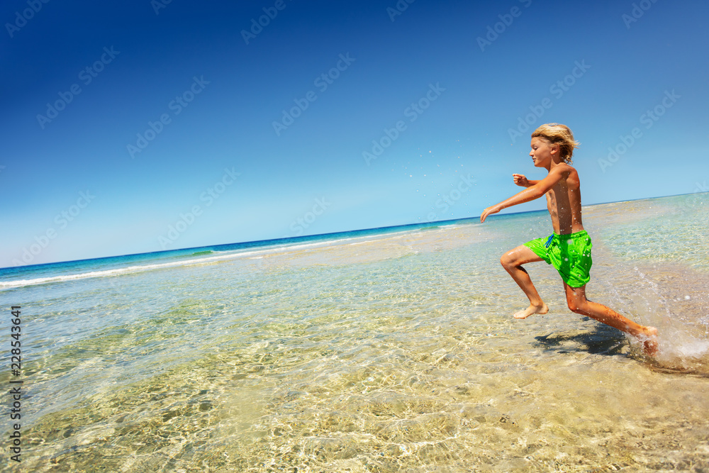 Boy running and splashing in shallow sea water