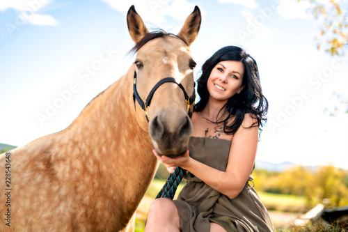 A Portrait of young beautiful woman with brown horse outdoors