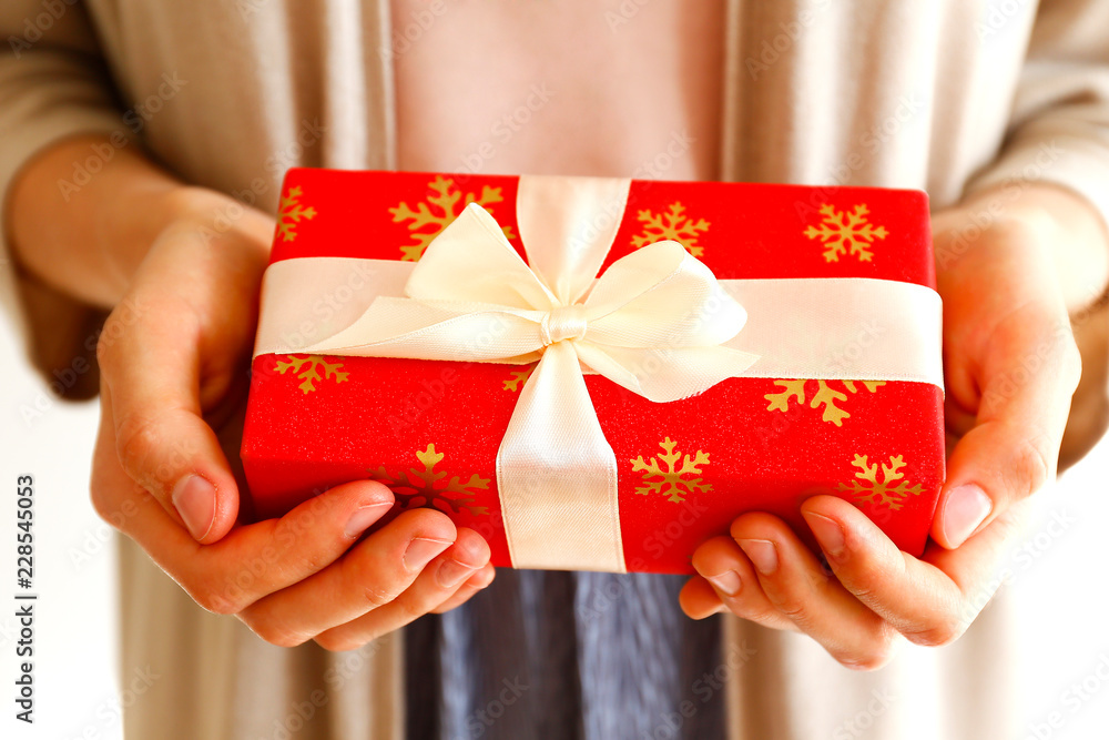 Young casual woman wearing pink shirt and long beige cardigan holding a beautiful present in shiny wrapping tied with golden bow. Giftwrapping concept. Background, copy space, close up. Young casual woman wearing pink shirt and long beige cardigan holding a beautiful present in shiny wrapping tied with golden bow. Giftwrapping concept. Background, copy space, close up.