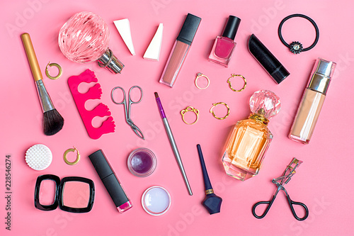 Set of cosmetics and accessories - lipstick, perfume, eye shadow, mascara, ring, nail polish, eyelash forceps, blush, earrings on pink background