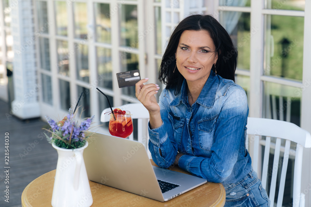 A beautiful young woman has a European appearance, holds a credit bank card in her hand, is happy that she can shop on the Internet, and pay for her orders. A beautiful young woman has a European appearance, holds a credit bank card in her hand, is happy that she can shop on the Internet, and pay for her orders.