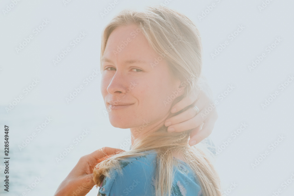 Close-up portrait of graceful blond woman in blue dress with sea in background Close-up portrait of graceful blond woman in blue dress with sea in background