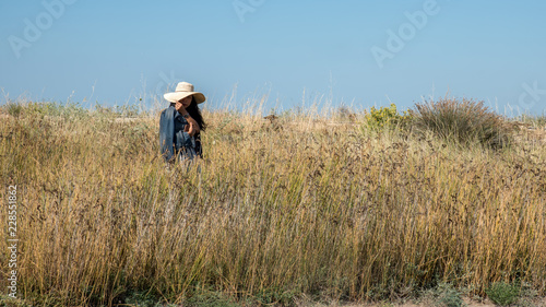 Woman standing on dry grassy hill holding her hat