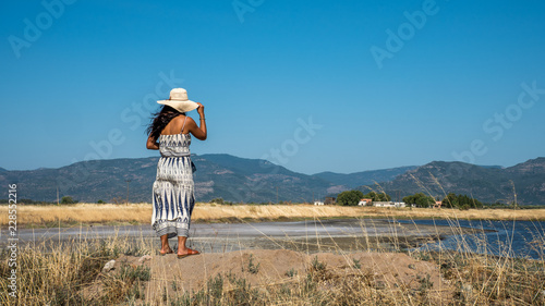 Woman standing on hill holding hat and looking at village in distance