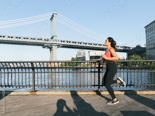 Photography Young athletic woman jogs along the water in New York City