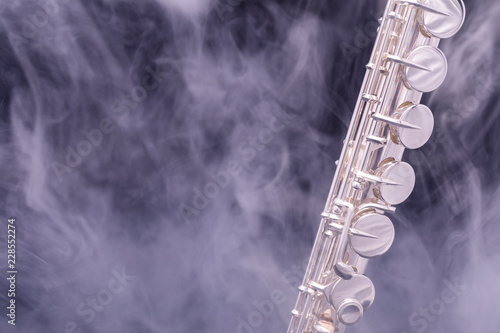 A silver plated alto flute in smoke on a black background