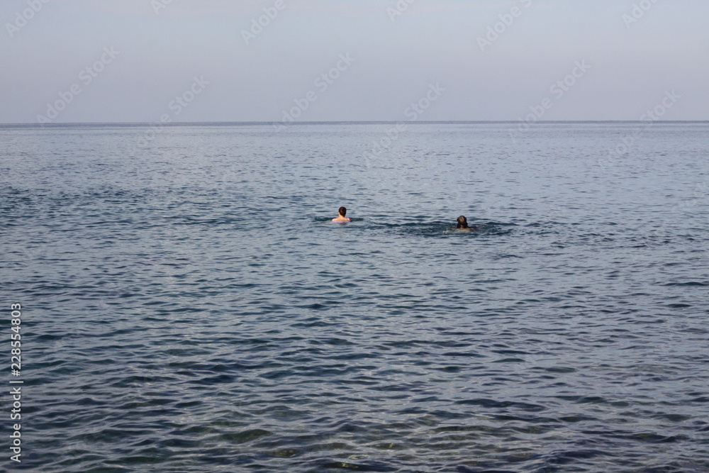 Two swimmers with faces not seen in an open see swimming to a horizon