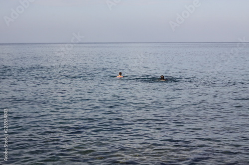 Two swimmers with faces not seen in an open see swimming to a horizon