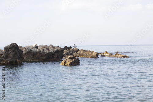 Fishermen standing on rocks with rods in a small bay of Mediterranean sea