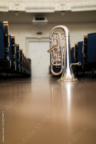 A euphonium standing on its bell on the floor amongst rows of chairs photo