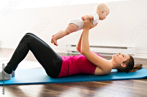 Fototapeta Naklejka Na Ścianę i Meble -  A Portrait of beautiful young mother in sports wear with her charming little baby in training session