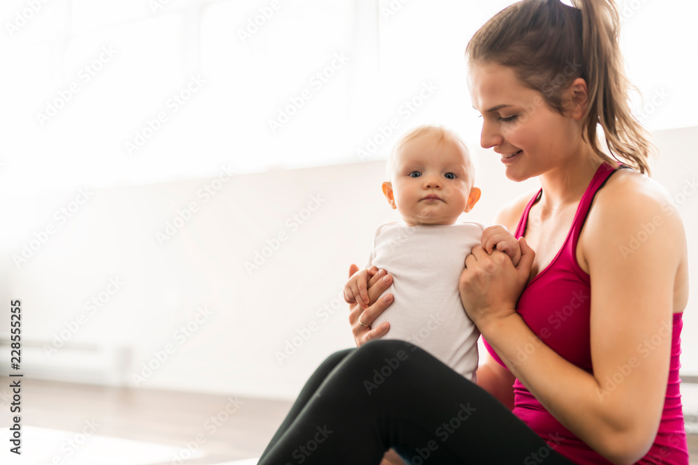 A Portrait of beautiful young mother in sports wear with her charming little baby in training session A Portrait of beautiful young mother in sports wear with her charming little baby in training session