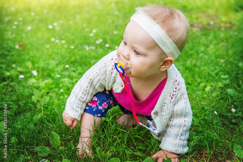 Baby girl sitting on the grass, sucking a pacifier. Baby girl sitting on the grass, sucking a pacifier.