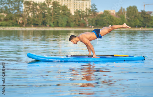 Man practicing yoga, doing balance body weight smimming on paddle board. © serhiibobyk