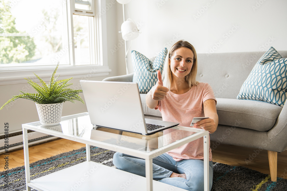 Happy woman with a credit card and a laptop on sofa at home