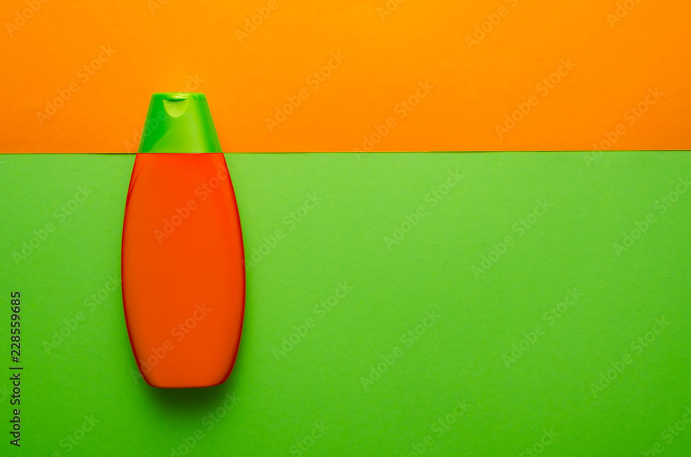 Vertical. Orange and green bottle of shampoo on the background of the same colors Vertical. Orange and green bottle of shampoo on the background of the same colors