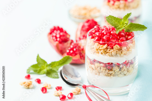 Pomegranate parfait - sweet organic layered dessert with granola flakes, yogurt and red ripe fruit seeds.