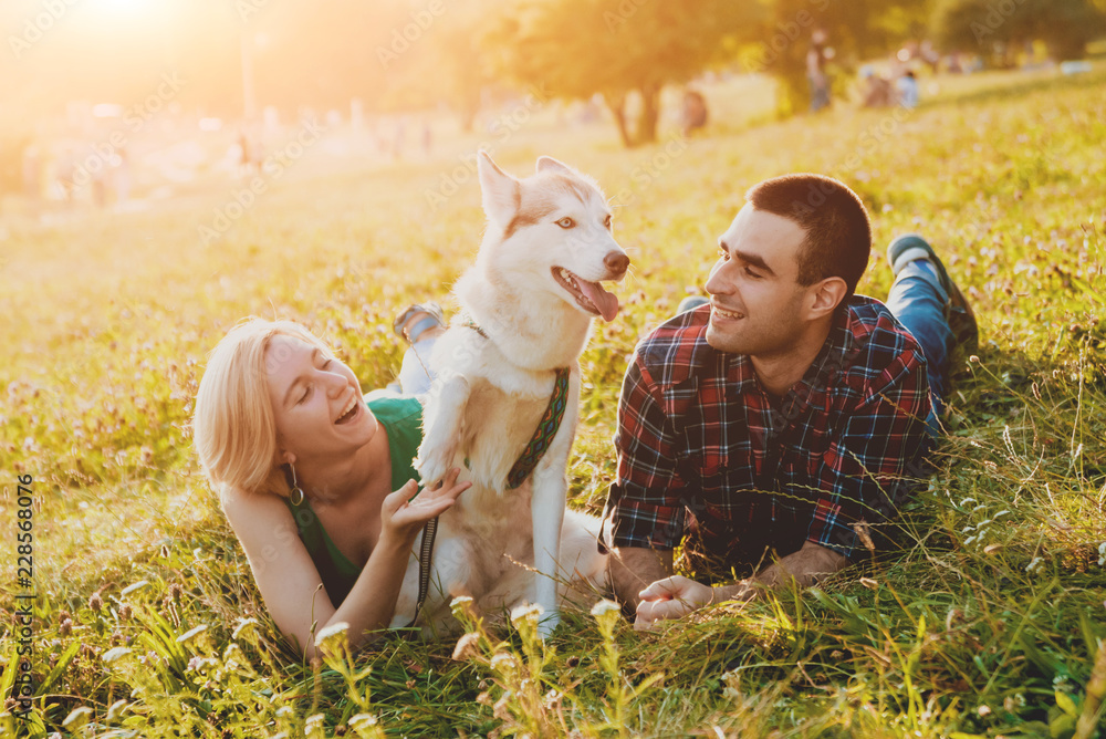Fototapeta premium Dog with owners spend a day at the park. Young couple and husky running, playing and having fun.