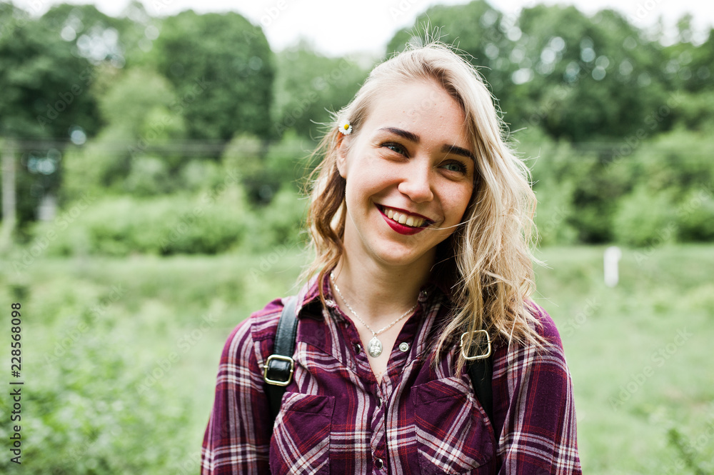 Close-up portrait of a smiling blond girl in tartan shirt in the countryside.