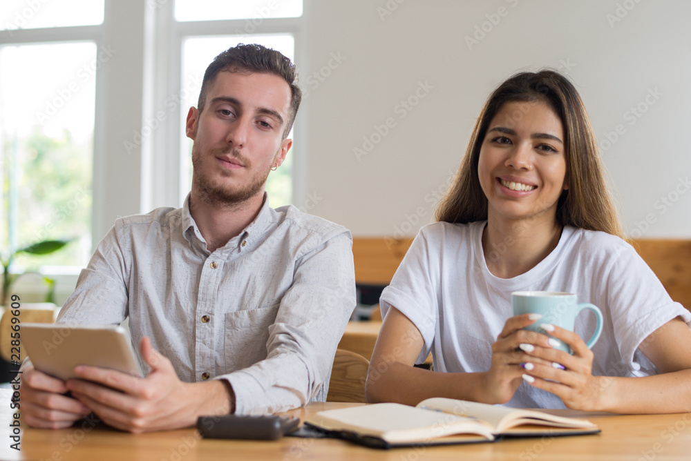 Students studying and relaxing in cafe. Young man and woman sitting at table and looking at camera. Friendship and education concept. Front view. Students studying and relaxing in cafe. Young man and woman sitting at table and looking at camera. Friendship and education concept. Front view.