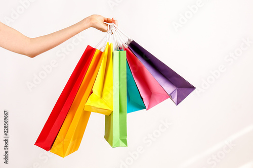 Cropped shot of female hand holding bunch of different colorful blank shopping bags over isolated white background. Many packets with in woman's arms. Black friday sale concept. Copy space, close up.