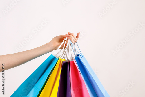 Cropped shot of female hand holding bunch of different colorful blank shopping bags over isolated white background. Many packets with in woman's arms. Black friday sale concept. Copy space, close up.