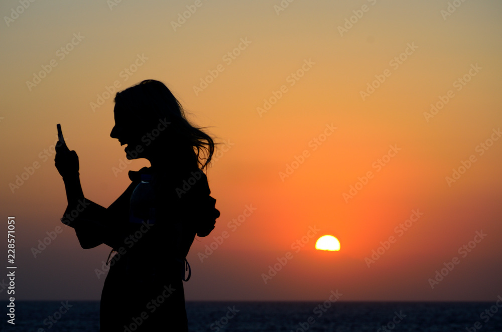 Silhouette of a woman with mobile phone during sunset.