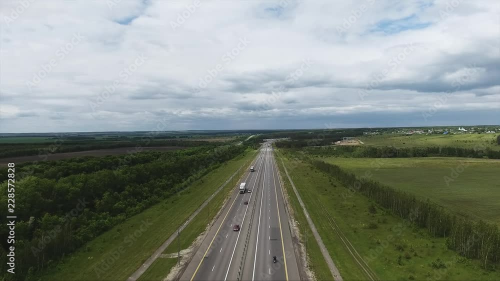 Beautiful drone view of riding cars, trees, long wide road surrounded by large green fields in rural area under clouded sky on summer day. Beautiful drone view of riding cars, trees, long wide road surrounded by large green fields in rural area under clouded sky on summer day.