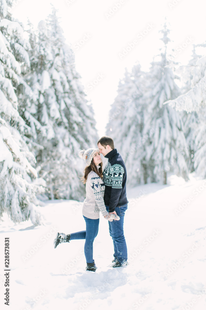 happy loving couple walking in snowy winter forest, spending christmas vacation together. Outdoor seasonal activities. Lifestyle capture.