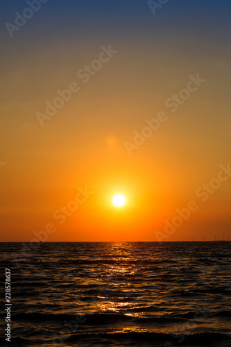Bright sunset with large yellow sun under the sea surface. Sunset over sea landscape. Beautiful sunset with sky over calm sea in tropical island © kanpisut