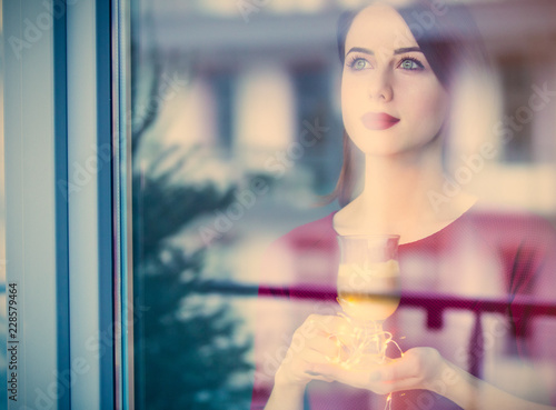 Beautiful rednead woman with cup of coffee or cappuccino near a window reflection photo