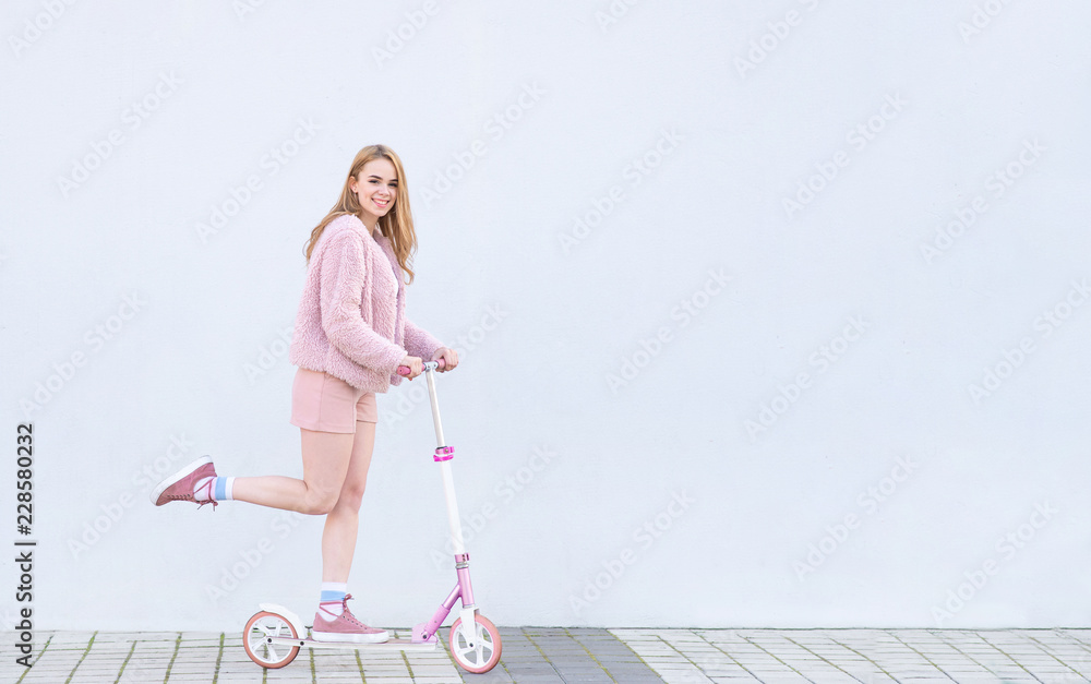 Φωτογραφία Happy, fashionable girl in pink clothes rides on a pink kick scooter, looks into the camera and smiles, isolated on a white background