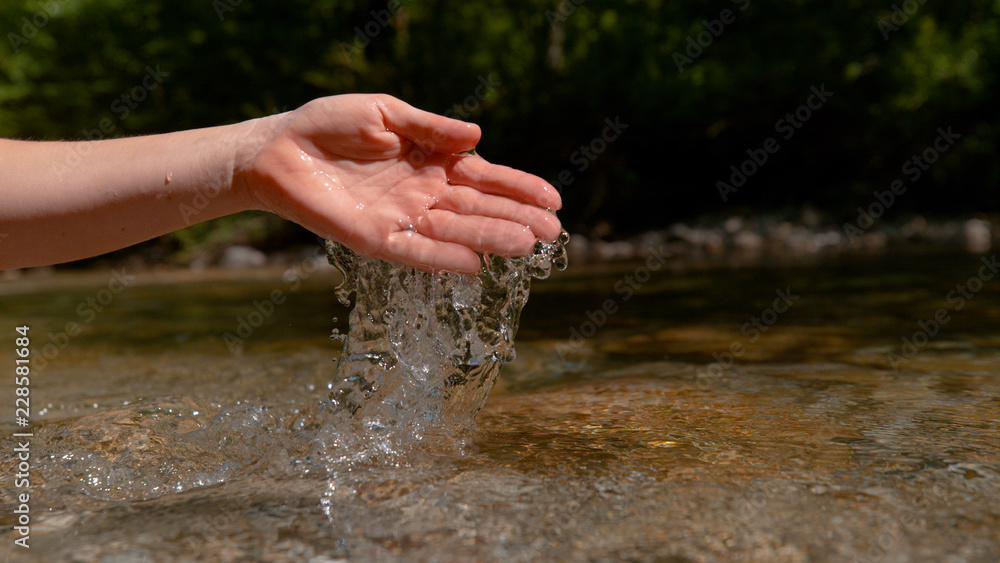 COPY SPACE: Unknown girl scoops up a handful of water from a tranquil brook.