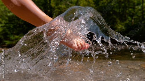 CLOSE UP: Unrecognizable playful girl splashing the glassy water with her foot.