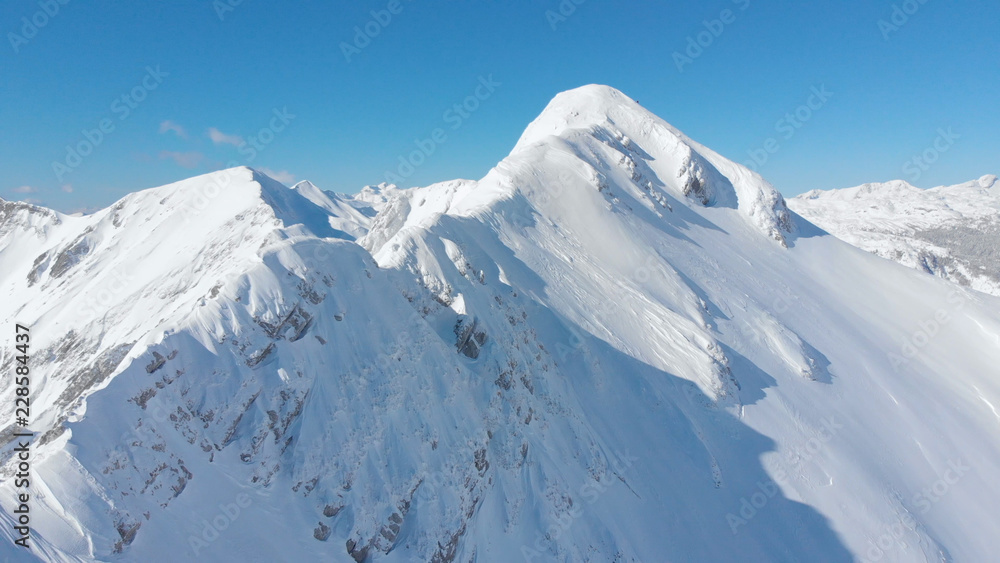AERIAL: Cinematic shot of a majestic snowy mountain ridge in the sunny Alps.