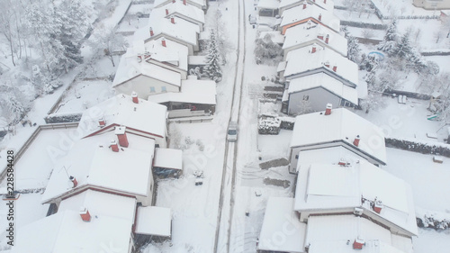 AERIAL: Silver car driving down the snowy road leading through the suburbs. © helivideo