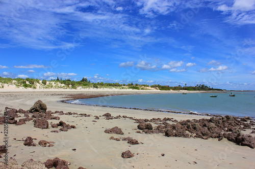 Carnaubinha Beach, Lupis Correia, Piauí: sunny day, deserted beach, blue sky with clouds, rocks, boats.
