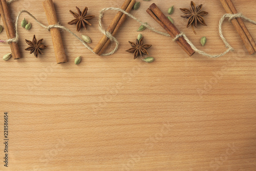 Decoration spices with space for text: cinnamon, cardamom, anise, tied with a rope on the background of a wooden board