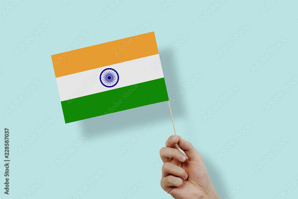 A hand holding the flag of India on a pastel blue background. India flag held in your hand. The concept of voting, manifesting, expressing one's own views. An Indian citizen, patriotism. A hand holding the flag of India on a pastel blue background. India flag held in your hand. The concept of voting, manifesting, expressing one's own views. An Indian citizen, patriotism.