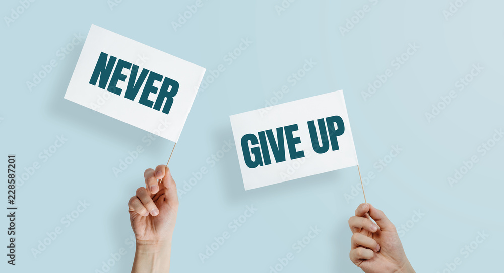 Two hands lift up the white flags with the word NEVER GIVE UP. The concept of fighting, not giving up. Getting strength and motivation to act. Fight with yourself. Two hands lift up the white flags with the word NEVER GIVE UP. The concept of fighting, not giving up. Getting strength and motivation to act. Fight with yourself.