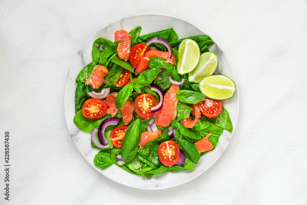Salmon salad with spinach, cherry tomatoes, red onion, lemon and basil in a plate over white marble background Salmon salad with spinach, cherry tomatoes, red onion, lemon and basil in a plate over white marble background