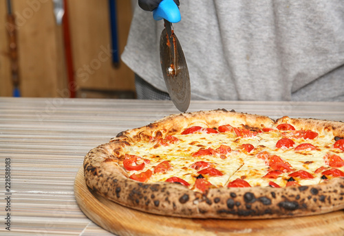 Professional chef cutting Italian oven baked pizza in restaurant, closeup