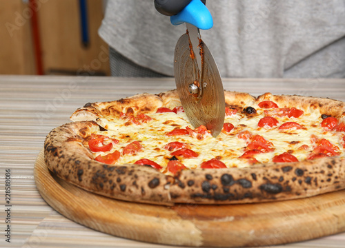 Professional chef cutting Italian oven baked pizza in restaurant, closeup