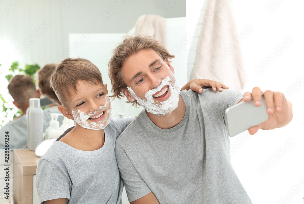 Father and son taking selfie with shaving foam on faces in bathroom