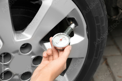 Woman checking car tire pressure with air gauge, closeup